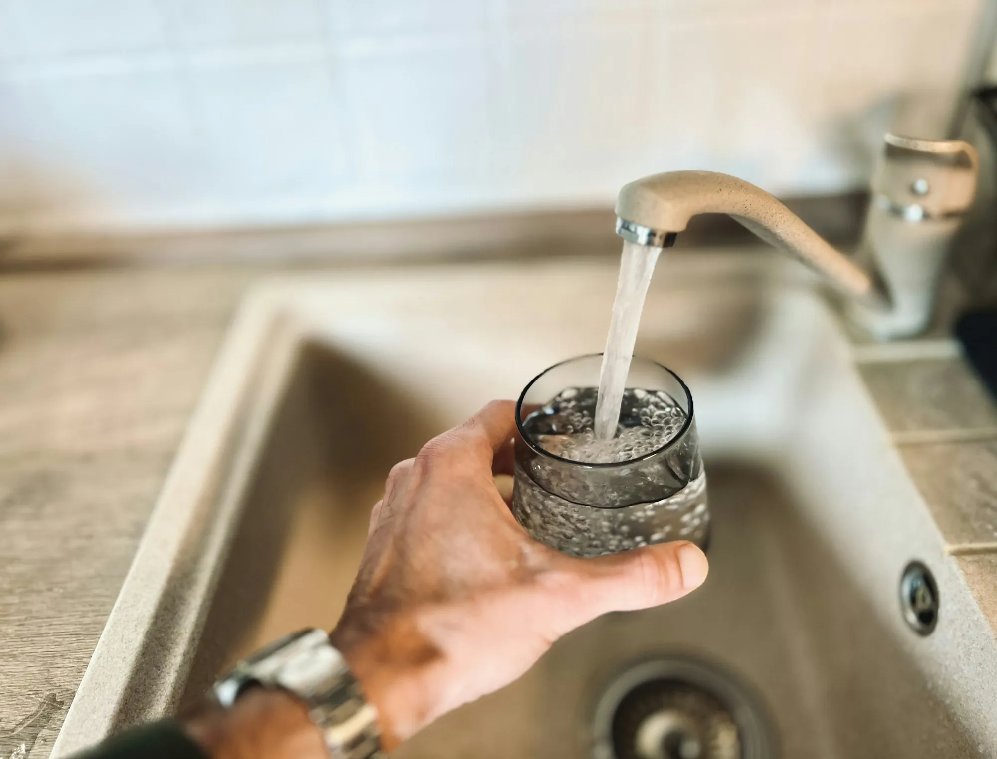 Water Filtration in Newport Beach Built Around What Your Water Actually Needs Hand holding a glass of water under a kitchen faucet